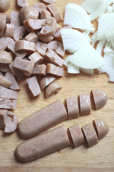 Cut up onion and sausages on wooden cutting board