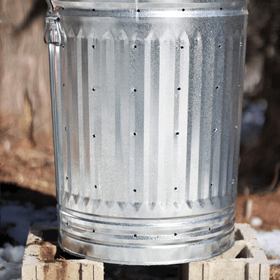 DIY compost bin made from a metal trash can sitting on top of two cinder blocks