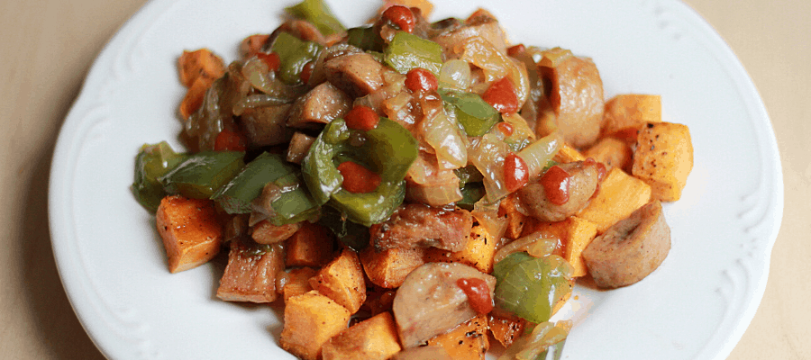 Sausage skillet with roasted sweet potatoes topped with sauteed chicken sausages, onions, & peppers with sriracha on top