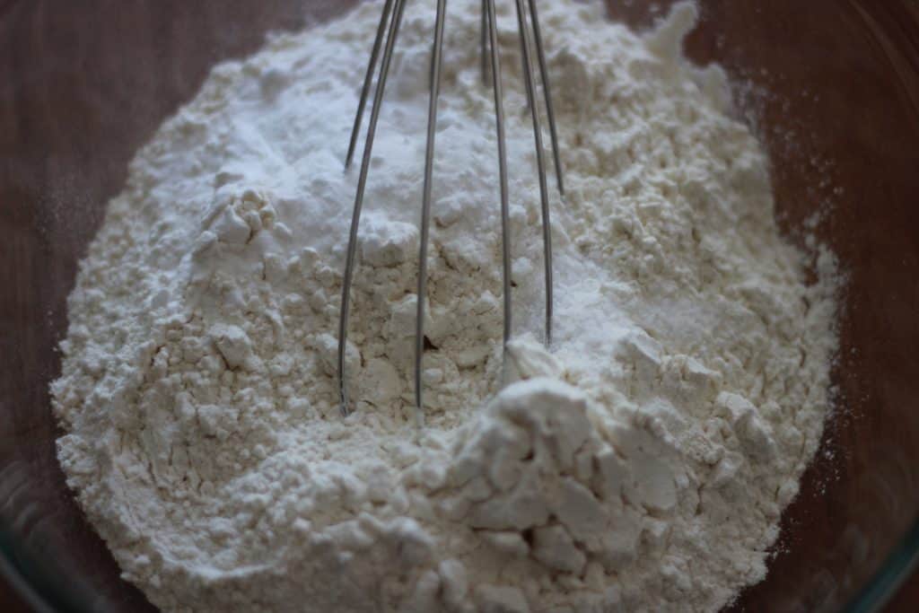 all-purpose unbleached flour, salt, and baking soda in a glass bowl with a metal whisk on top