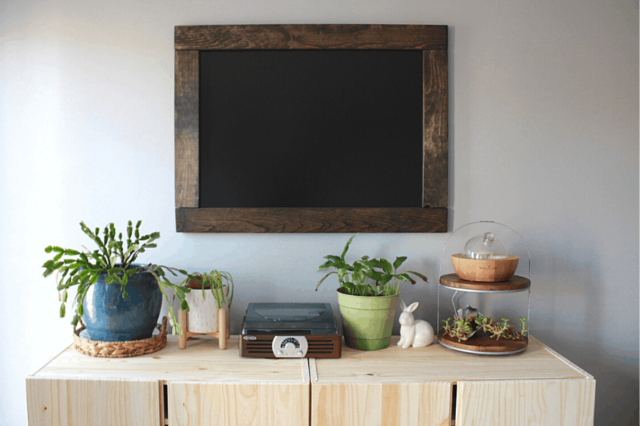 DIY chalkboard hanging on wall above wooden shelf with plants on it