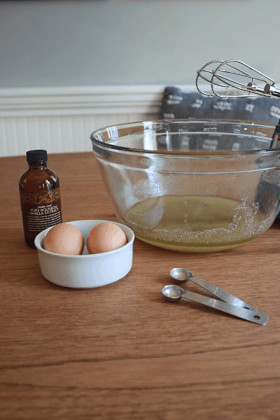 large bowl with sugar, brown sugar, avocado oil inside, with vanilla extract sitting on the table with two eggs inside a small white bowl