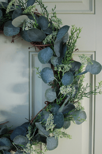 close up image of DIY eucalyptus wreath hanging on a light green front door