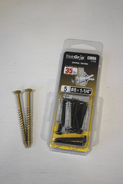 two 2'' wood screws laying on a table next to a package of drywall anchors