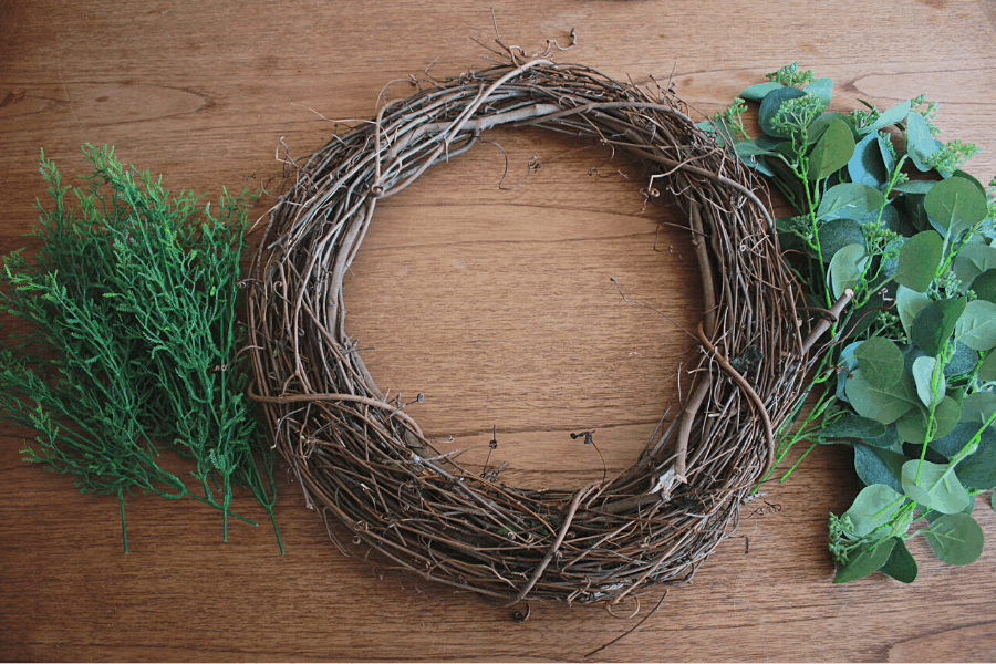 grapevine wreath, eucalyptus stems, and grass stems laid out on a wooden table