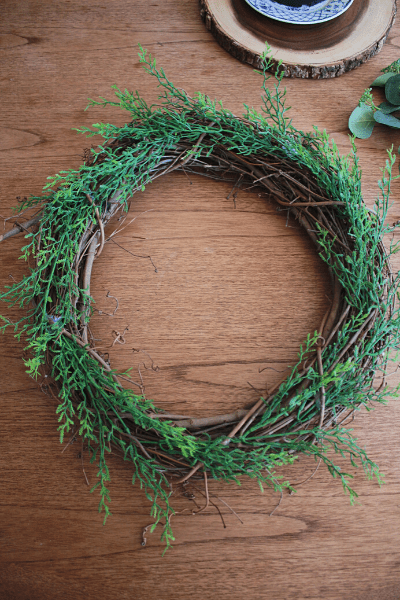 grapevine wreath with leaf bush stems tucked in and hot glued into place around it