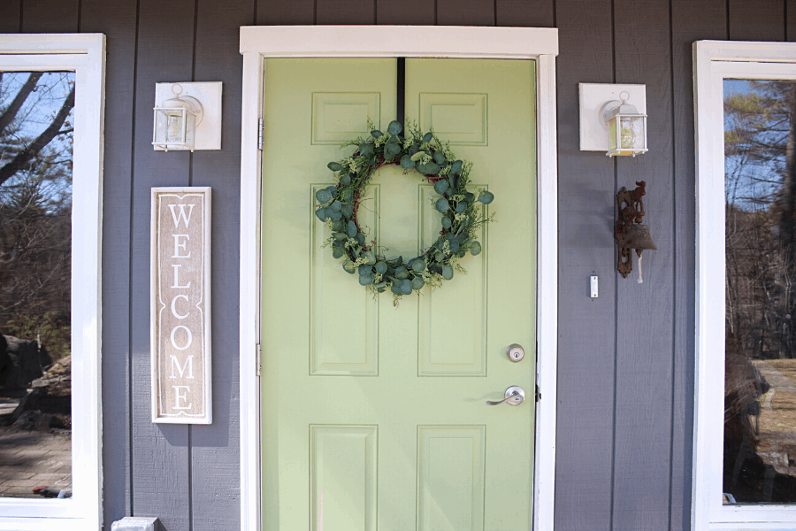 green front door with DIY eucalyptus wreath on it and welcome sign handing on the house to the left