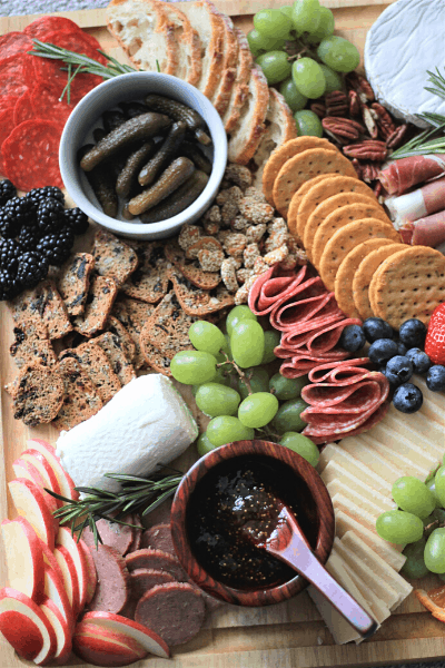 variety of meats, cheeses, crackers, fruits, and pickles on a wooden board