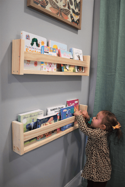 toddler getting a book out of a diy ikea children's bookshelf hanging on the wall 