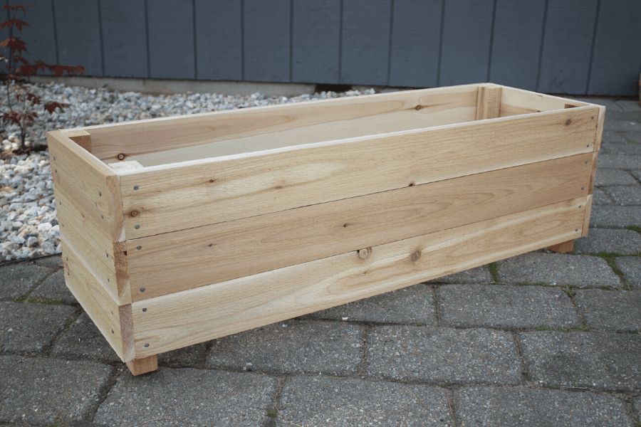 cedar DIY planter box sitting on top of cement pavers