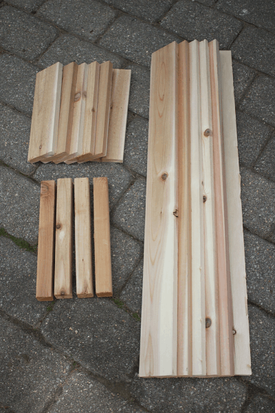 three different piles of cut wood with different lengths laying on cement pavers