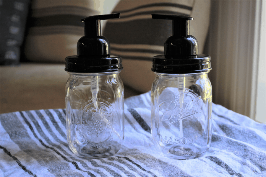 two foaming hand soap dispensers sitting on a gray and white dish towel