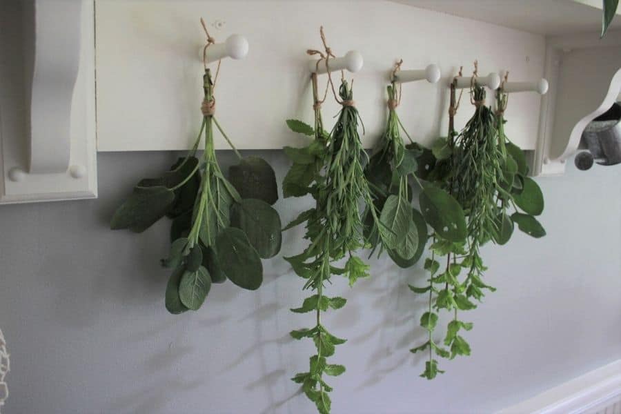 sage, mint, and rosemary bundles hang drying on a peg rail shelf