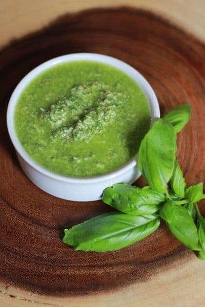 small white bowl of pesto with fresh basil sitting next to it on a wooden round cutting board