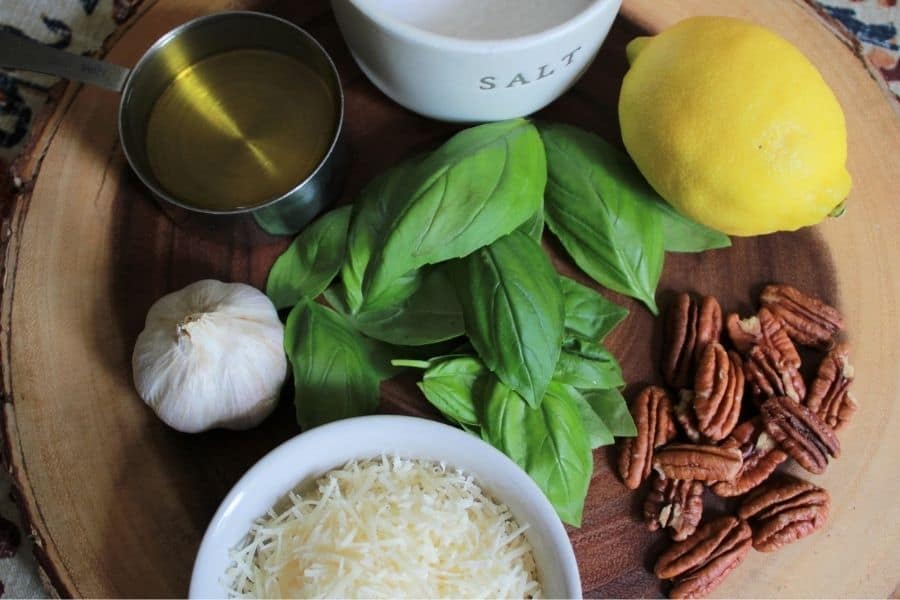 ingredients for easy pesto recipe spread out on a round wooden cutting board