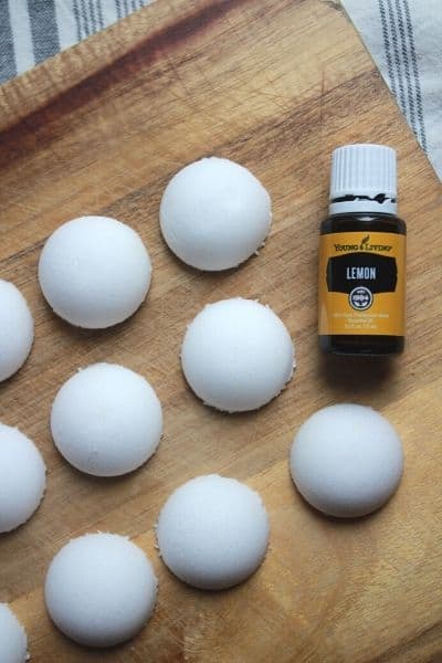 non-toxic toilet cleaning bombs lined up on a wooden cutting board with a bottle of young living lemon essential oils laying next to them