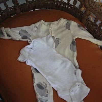 baby clothes lying on a burnt orange cushion in a wicker bassinet